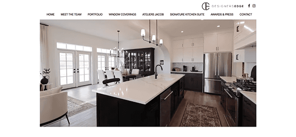 Modern kitchen with a large island, marble countertops, dark cabinets, and pendant lighting reminiscent of the sleek designs you might find on the best carpenter websites. A dining area with white chairs is visible, and large windows provide ample natural light.