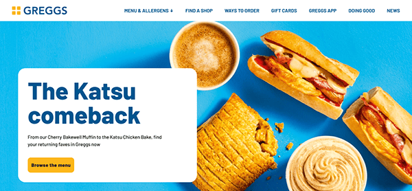 Greggs promotional banner on the best cafe websites showcases the Katsu Chicken bake, sausage roll, muffins, and dip. The text reads "The Katsu comeback." A sleek cafe design accompanies the menu navigation at the top.