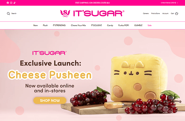 Ad for IT'SUGAR featuring a "Cheese Pusheen" plush toy next to grapes and cheese on a wooden board. Discover this adorable treat at one of the best candy destinations, available both online and in-store.