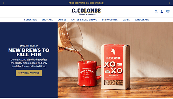 Coffee cascades into a red mug beside a box of La Colombe XOXO coffee beans on a wooden surface, reminiscent of the premium brews featured on the best cafe websites. Promotional text enhances the cozy scene, inviting you to explore and savor.