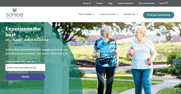 Two elderly women stroll through a park, water bottles in hand, enjoying the vibrant atmosphere. Discover Sonida Senior Living's unparalleled services and amenities by exploring the best assisted living websites today.
