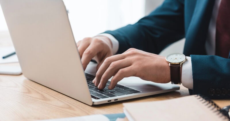 A person in a suit is typing on a laptop at a wooden desk with a notebook nearby, likely crafting the next high-converting Wix site.