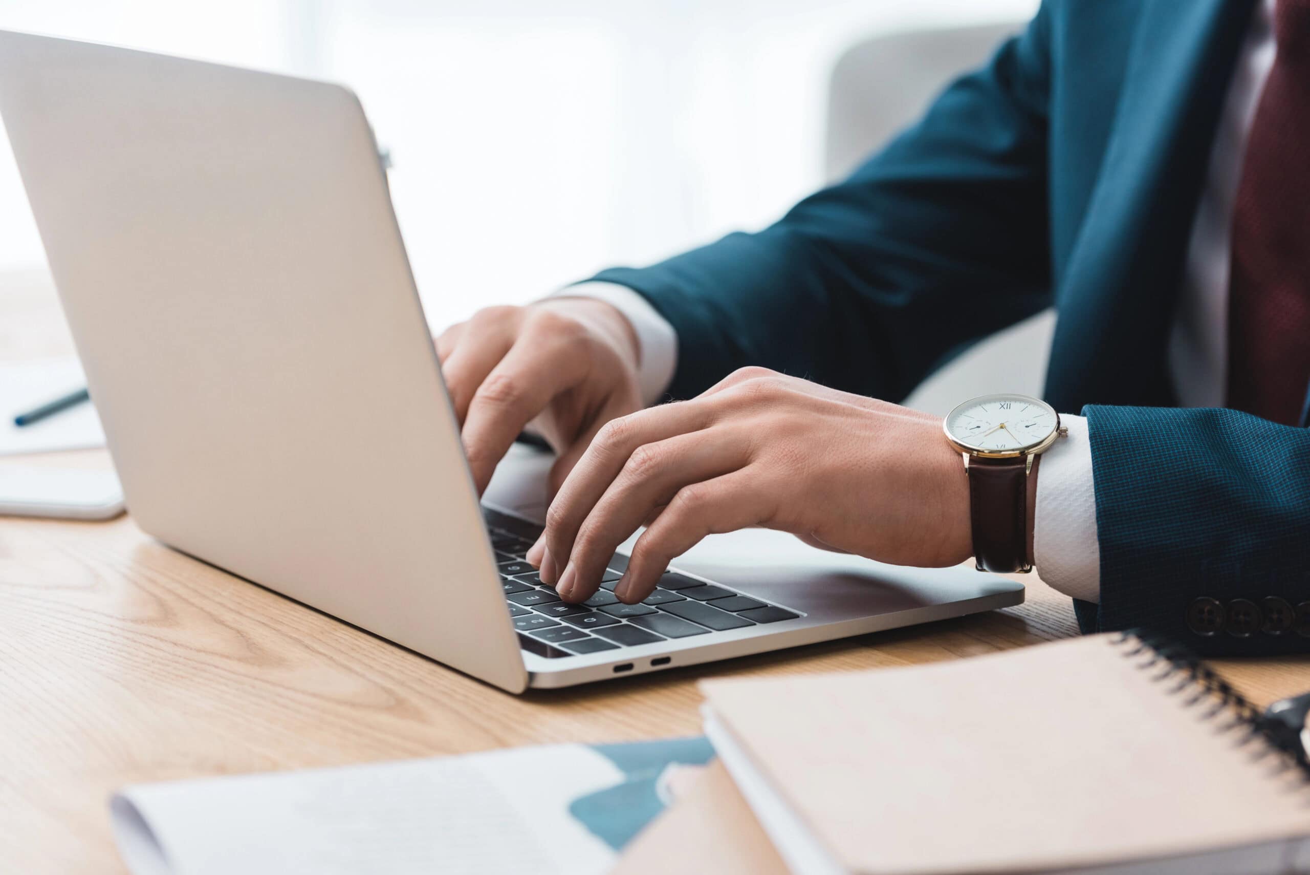 A person in a suit is typing on a laptop at a wooden desk with a notebook nearby, likely crafting the next high-converting Wix site.