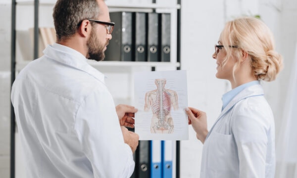 Two people in lab coats discuss a medical diagram of human anatomy, strategizing near a shelf filled with binders. Their insightful exchange resembles photographers analyzing the perfect shot to increase exposure in their field.