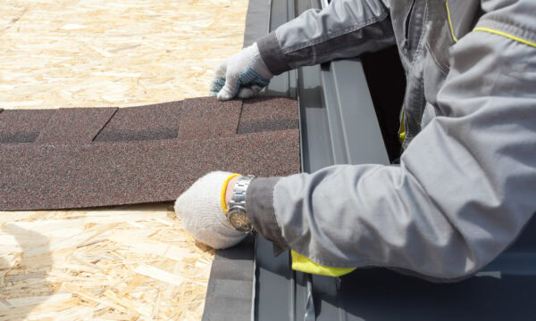A person wearing gloves expertly installs shingles on a roof with a wooden base, showcasing their roofing skills.