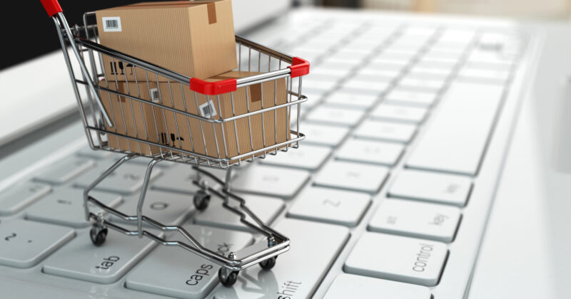A small shopping cart with cardboard boxes sits on a computer keyboard, symbolizing ecommerce and online sales.