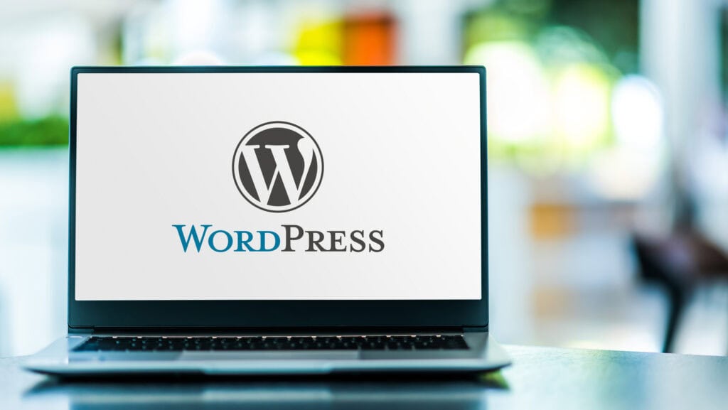 A laptop screen showcases the WordPress logo, featuring the iconic stylized "W" with "WordPress" beneath it, set against a blurred background. Ideal for those diving into website design and eager to harness the power of this versatile platform.