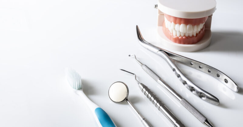 Dental tools and a toothbrush are arranged next to a model of teeth on a white surface, showcasing the essentials for effective dental marketing.