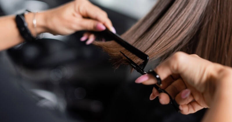 Close-up of a hairdresser's skilled hands cutting brown hair with scissors and comb, showcasing the artistry that fuels hair salon growth.