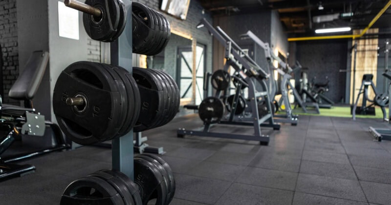 A gym featuring weights on racks and exercise machines set in a dark interior with rubber flooring, perfect for those inspired by cutting-edge fitness marketing.
