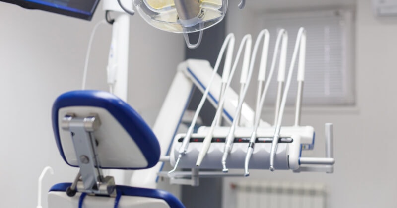 Dentist chair and overhead light in a dental clinic with various tools and equipment in the background.