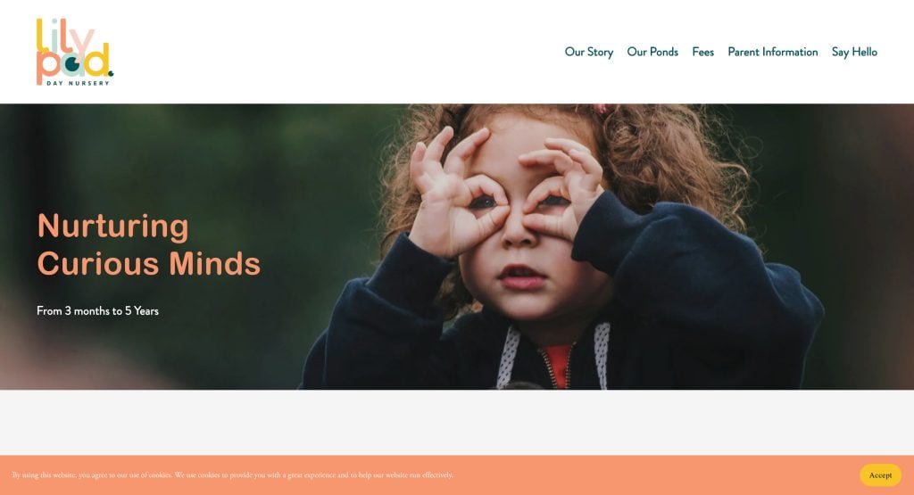 A young child makes playful glasses with their hands on their face. The text reads, Nurturing Curious Minds. From 3 months to 5 Years. The website header shows lily pod—an example of the best daycare websites, with a friendly menu and welcoming daycare website design.