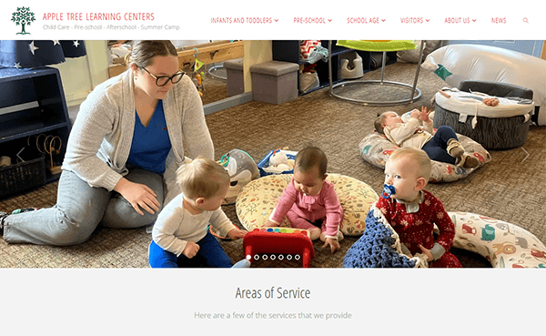 A caregiver engages with three babies playing on the floor in a vibrant daycare setting, surrounded by toys and cushions, capturing the essence of top-rated daycare websites.