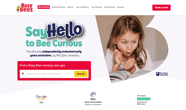 The Busy Bees website homepage, one of the best daycare websites, showcases a child reading. It features a search bar for nurseries, accreditation logos, and a convenient "Book a Visit" button.