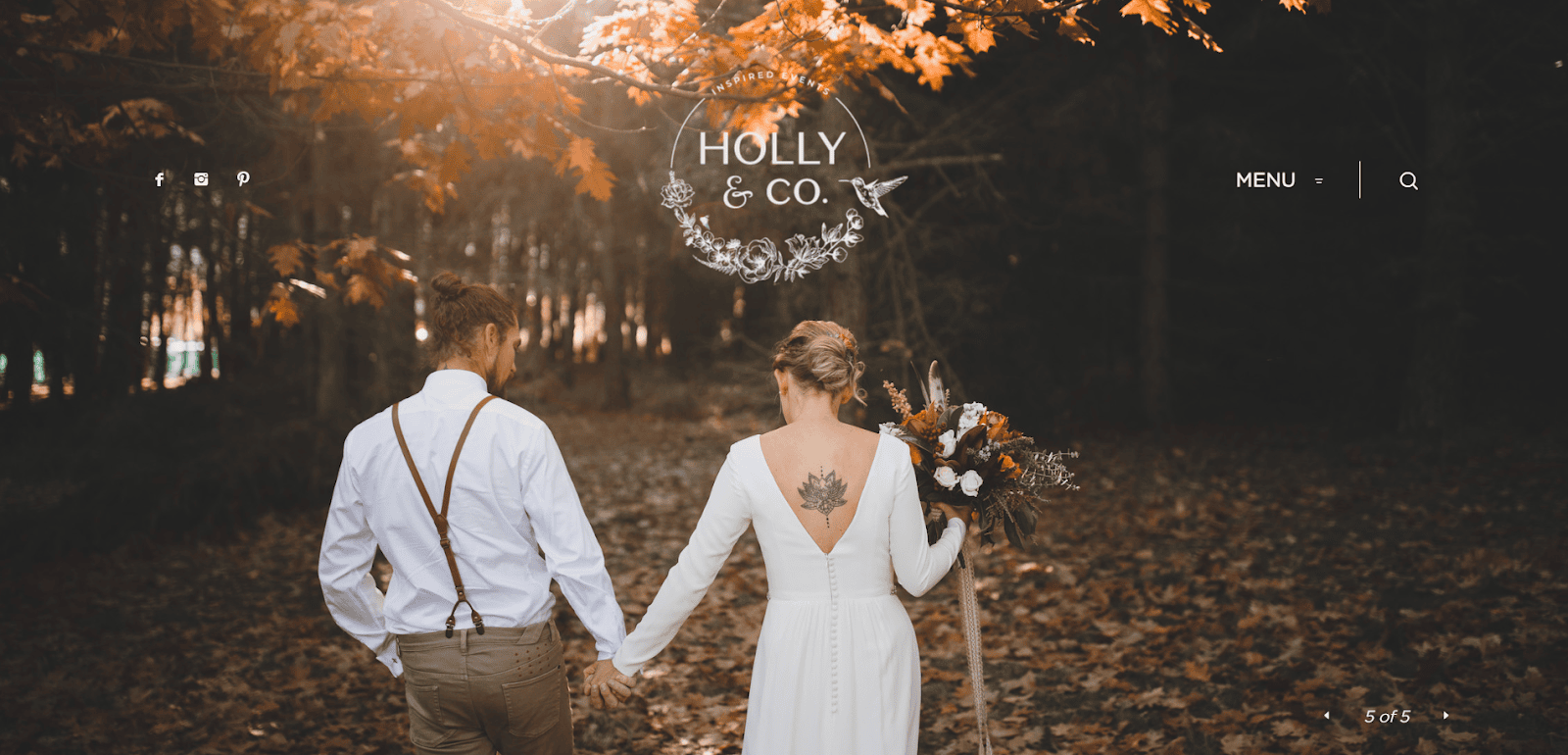 A couple, seen from behind, walks hand-in-hand in a sunlit autumn forest. Perfect inspiration for Best Event Planners, the woman in a white dress holds a bouquet as warm sunlight filters through colorful leaves above.