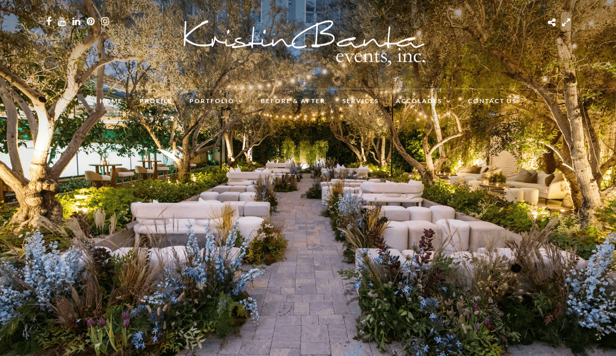 A beautifully decorated outdoor event space with white sofas, lush greenery, string lights overhead, and floral arrangements, set for a gathering at night. Perfect inspiration for event planner websites. Kristin Banta Events, Inc. is displayed across the top.