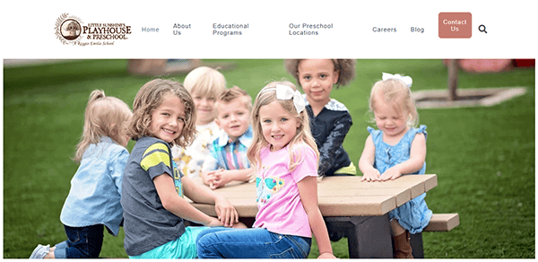 Children smiling at a picnic table on a playground, enjoying the lively atmosphere of daycare.