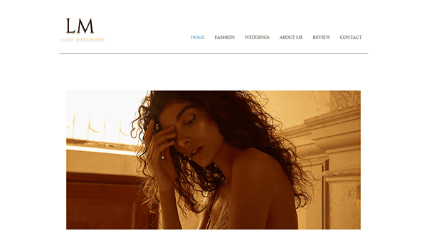 A woman with curly hair poses with her hand on her forehead, eyes closed, in warm lighting. The webpage, ideal for best hair stylist showcases, features a navigation menu with sections like Fashion and Weddings.