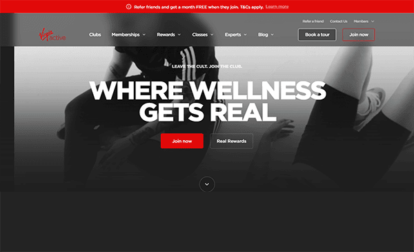 Gym website homepage with bold text "WHERE WELLNESS GETS REAL" on a grayscale image background. Red accents highlight navigation and call-to-action buttons like "Join now" and "Real Rewards." Discover why it's among the top gym websites designed for those who live to move.