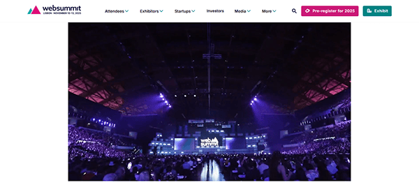 A large audience fills an indoor arena for a web summit event, with purple lighting and a stage displaying the event's logo, showcasing one of the best conference websites.