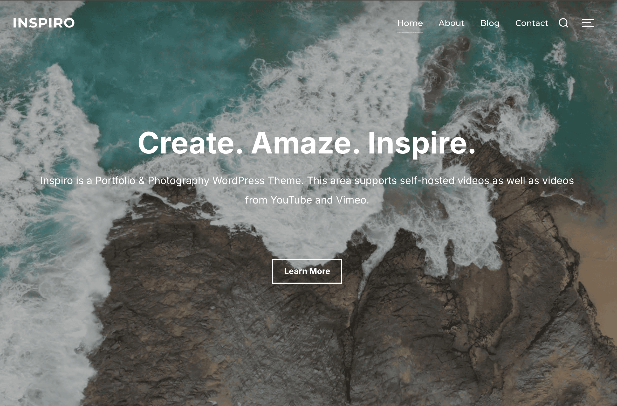 Aerial view of waves crashing on rocky shore with text overlay: "Create. Amaze. Inspire." Above is a site menu; below is a button labeled "Learn More.
