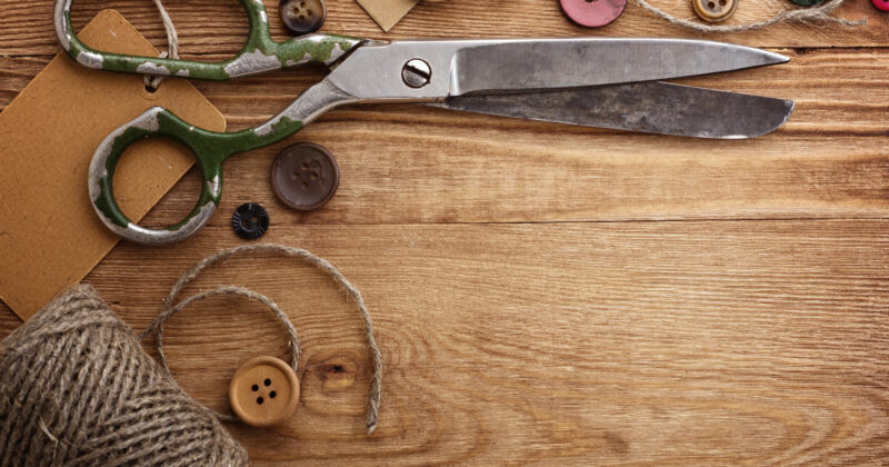A pair of vintage scissors, twine, buttons, and brown tags arranged on a wooden surface—perfect inspiration for browsing the best vintage clothing websites.
