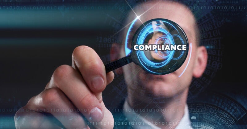 A person holds a magnifying glass with the word "COMPLIANCE" in focus, surrounded by digital patterns and binary code.