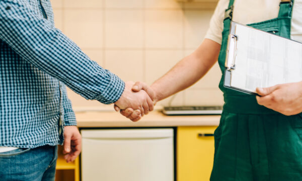 Two people shake hands in a kitchen—one in a checkered shirt and jeans, the other in green overalls with a clipboard—signifying a successful connection with a local customer that matches their ideal client profile.