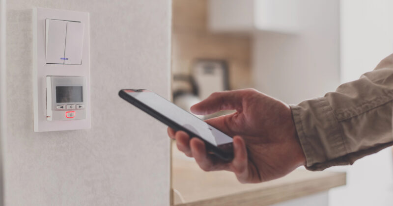 A person uses a smartphone to control a smart thermostat mounted on a wall, showcasing the convenience of the best smart home technology in a modern home.