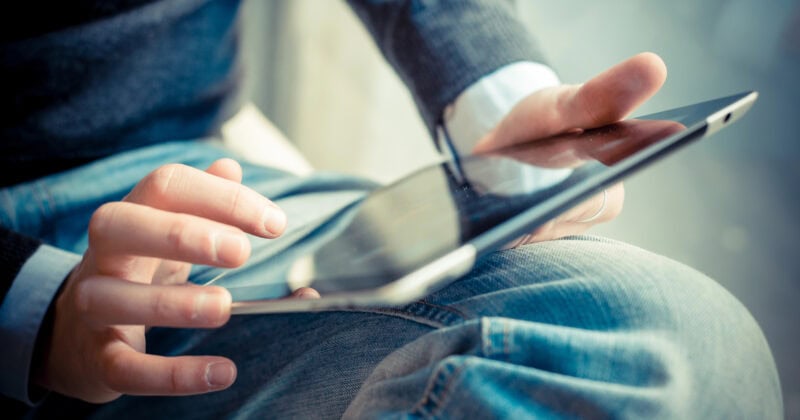 A person sits cross-legged while using a tablet device, touching the screen with one hand and holding the device with the other.