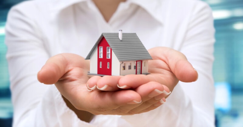 A person in a white shirt holds a small model house in their open hands, symbolizing real estate or home ownership—ideal imagery for 2025 Real Estate Websites or modern WordPress Themes.