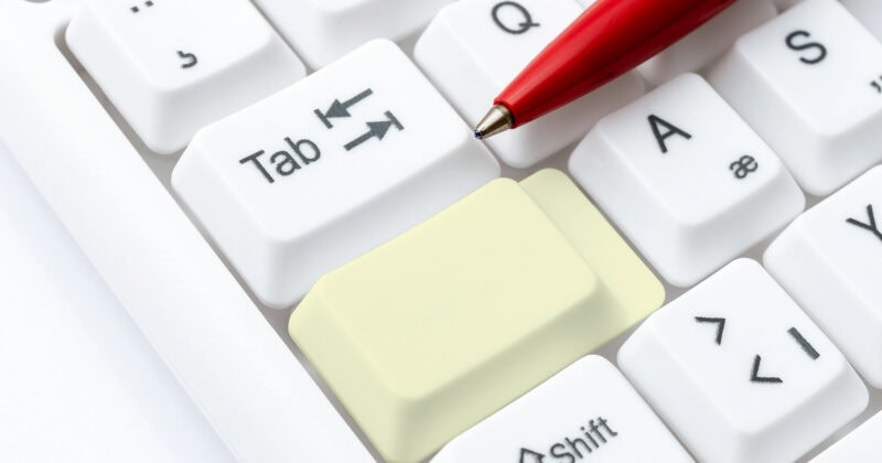 A computer keyboard with a red pen placed diagonally across the keys showcases a unique blend of design inspiration. Among the white keys, a large yellow key between Tab and Shift stands out, much like a distinctive WordPress theme catching the eye of beginners.