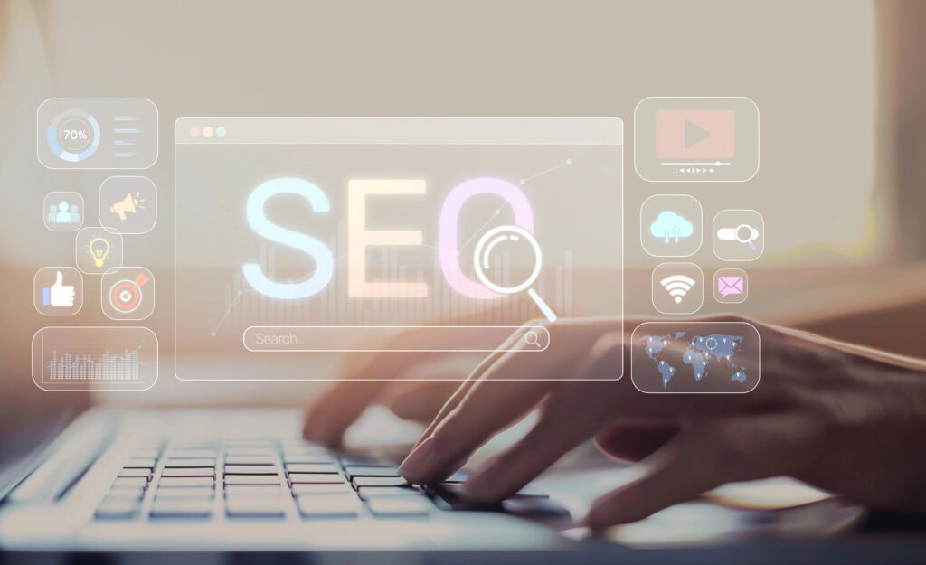 Hands typing on a laptop keyboard with a transparent overlay displaying the word "SEO" and various digital marketing icons.