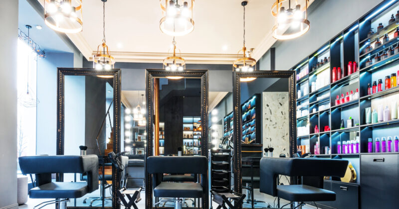 Modern hair salon interior with three styling stations, large mirrors, black chairs, pendant lights, and shelves filled with hair products—perfect inspiration for the best salon websites.