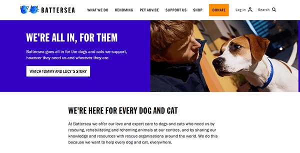 A man sits indoors looking at a brown and white dog. The Battersea website, one of the best pet adoption websites, promotes their support for dogs and cats in need, with navigation and a prominent "Donate" button shown.