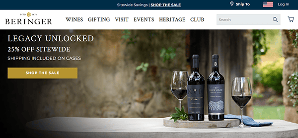 Two bottles of red wine and two filled glasses rest on a stone table outdoors, surrounded by a large beige wall and greenery—the perfect inspiration for top winery website design.
