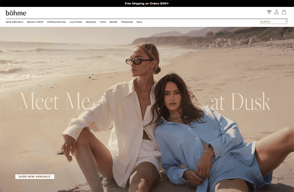 Two women wearing oversized button-up shirts sit on a sandy beach with cliffs and ocean in the background. Text on the image reads, "Meet Me at Dusk." Perfect inspiration for Best Small Business or creative small business websites.