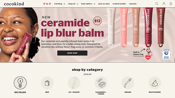 A woman smiles while holding a tube of cocokind ceramide lip blur balm. Five balm shades are displayed, with product details and a “Shop Now” button—echoing the clean, inviting style of the best small business websites—on a beige background.