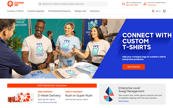 Four people wearing matching branded t-shirts sit and stand around a table with folded shirts. As one of the best T-shirt websites, this site makes it easy for businesses to create custom t-shirt designs.