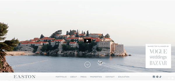 A small boat passes by a coastal island with red-roofed buildings surrounded by the sea, featured on one of the best wedding planner websites with navigation links and accolades.