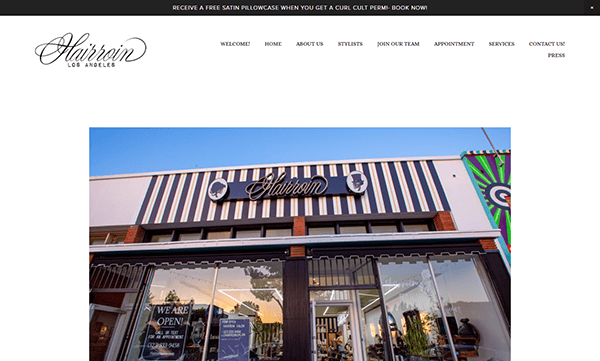 Front view of the Harriett Los Angeles salon with its black and white striped exterior, stylish signage, and "We Are Open" signs—an inspiring look for those seeking the best salon websites or unique salon website design ideas.