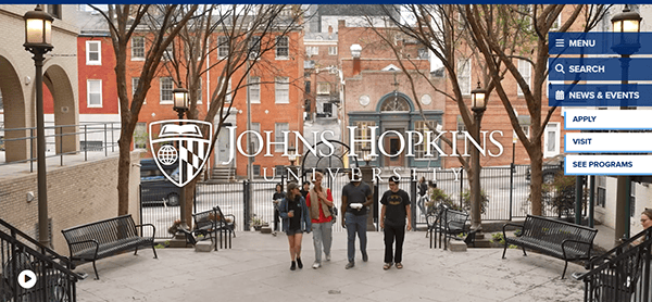 Students walk together on a campus pathway surrounded by benches and trees, with the Johns Hopkins University logo displayed prominently in the center—an inspiring scene often featured on top school websites.