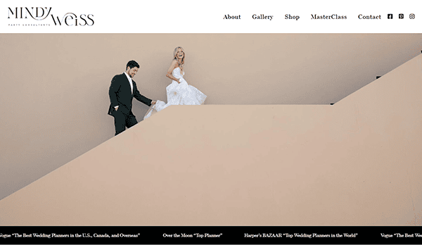 A bride and groom walk up a modern, angled staircase against a beige wall, hand in hand—capturing the kind of elegant moment often showcased on the best wedding planner websites.