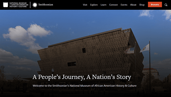 The Smithsonian National Museum of African American History and Culture, featured on many top museum websites, stands with the American and museum flags waving under a blue sky dotted with clouds.