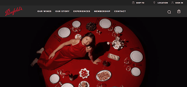 A woman in a red dress sits at a round red table set with wine glasses, plates, and various foods, viewed from above—an inviting scene reminiscent of the best winery websites and their elegant visual design.