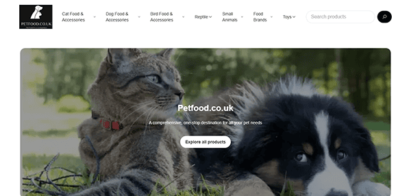 A cat and a dog lying together on grass, with the Petfood.co.uk website header and navigation menu—showcasing one of the best pet shop websites—visible at the top.