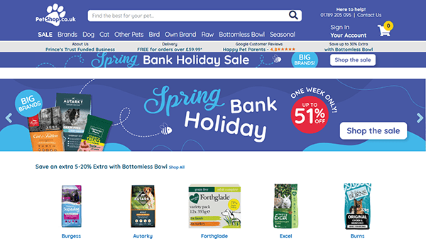 Screenshot of PetShop.co.uk homepage, one of the best pet shop websites, featuring a Spring Bank Holiday Sale banner with discounts up to 51% off and images of various pet food brands below.