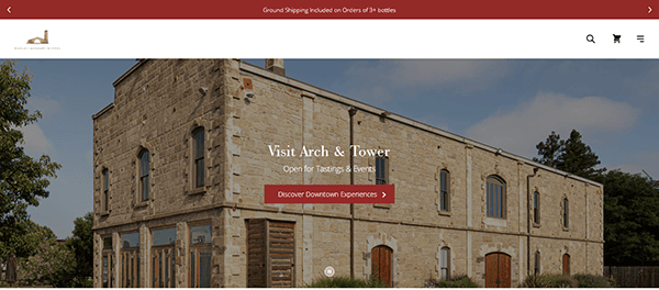 Stone building with arched windows and wooden doors; text overlay reads "Visit Arch & Tower - Open for Tastings & Events" with a button for downtown experiences—an example of standout winery website design.