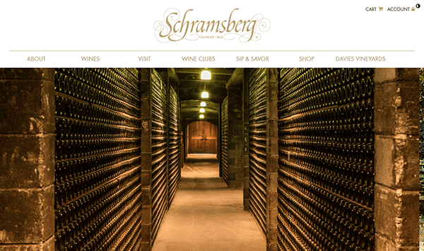A wine cellar with rows of wine bottles stacked on both sides, dimly lit by overhead lights, at Schramsberg Vineyards—a setting often featured on the best winery websites.