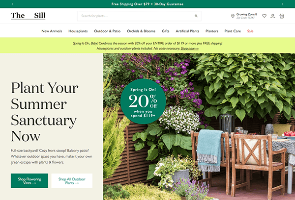 Outdoor dining table with wooden chairs set beside lush green plants and blooming flowers—perfect inspiration for the best small business websites. Enjoy a 20% off summer sale on The Sill’s outdoor plant collection!.